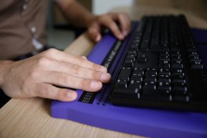 Blinde Person, die einen Computer mit Blindenschriftanzeige und einer Computertastatur benutzt. Blindenhilfe, Sehbehinderung, Konzept des unabhängigen Lebens.